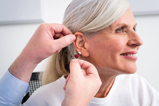 Ältere Frau bekommt ein modernes Hörgerät angepasst und lächelt zufrieden dabei.